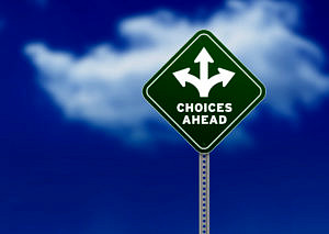 Bild zeigt blauen Himmel mit Wolken. Davor sieht man ein dreieckiges Schild mit der Aufschrift "Choices ahead"